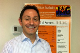 Jason Moore, director of operations at JAG, stands next to a chart showing positive outcomes for students in the program.