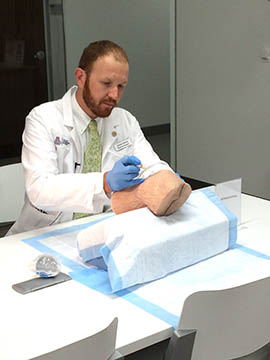 Second-year medical student James Gentry practices using a needle to remove fluid from a synthetic knee manufactured by SynDaver Labs.