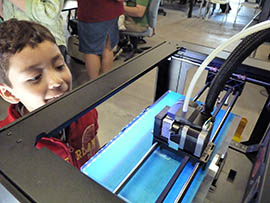 Giovanni Davien looks on as a 3D printer makes a hair comb out of white plastic.