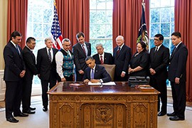 President Barack Obama signs H.R. 205, the HEARTH Act of 2012, loosening federal restrictions on leasing of tribal lands, while government and tribal officials look on in the Oval Office look on in June 2012.